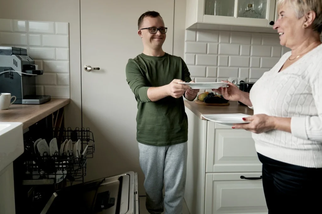 Disabled man with down syndrome unpacking dishwasher with support worker