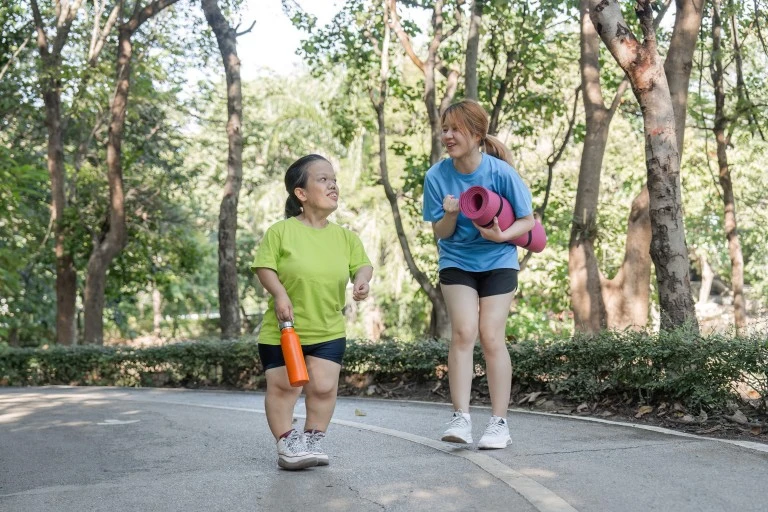 Disabled woman with friend going for a walk in the park with yoga mats