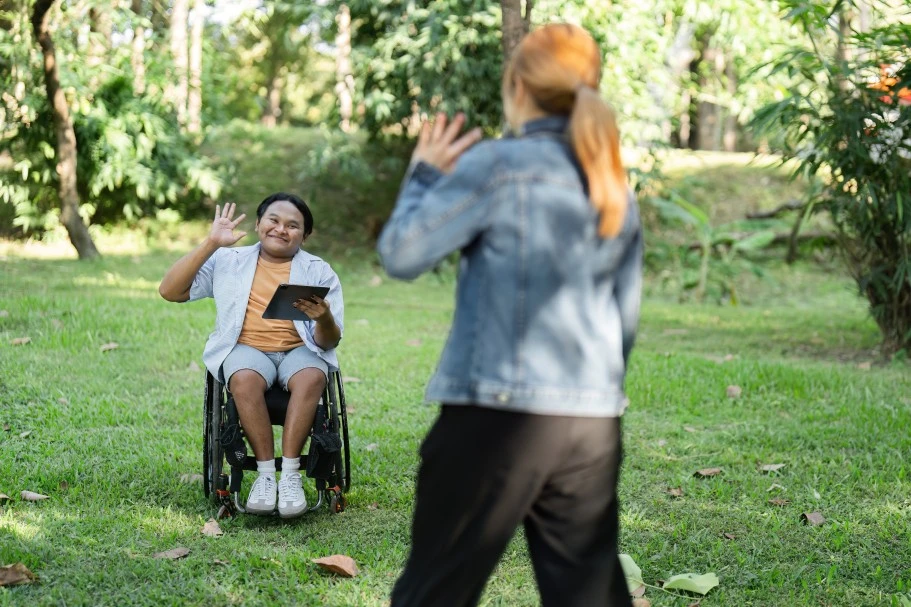 Disabled man in wheelchair waving at friend in park