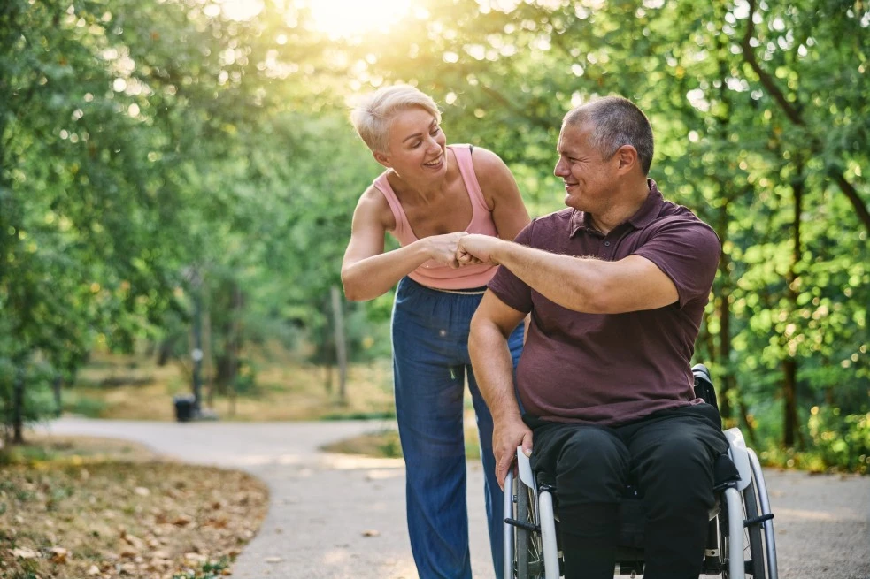 Disabled man in wheelchair fist pumping support worker while outside in park